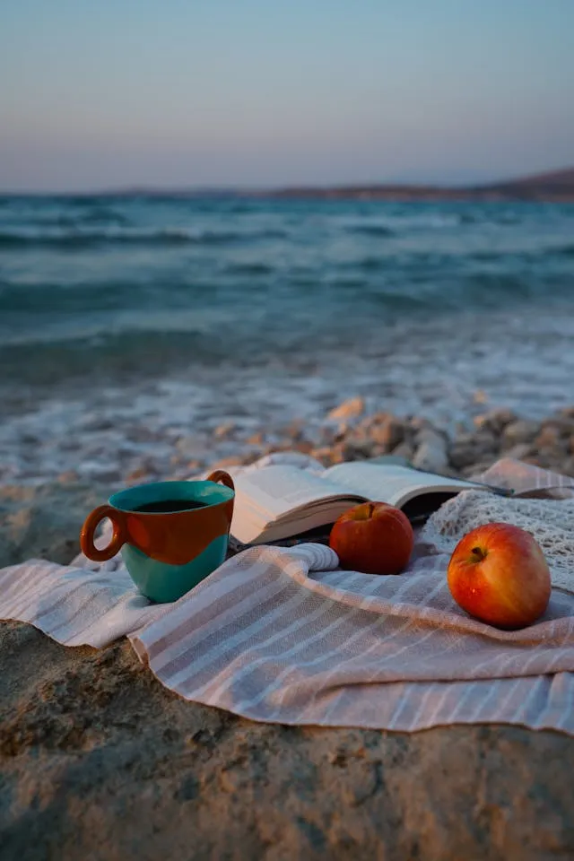 Two apples and a cup on a towel on the beach.